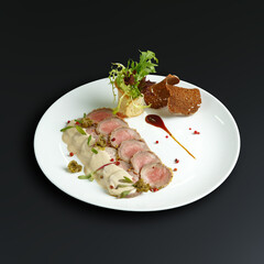 traditional dishes of European cuisine, delicacy, banquet snack. culinary dishes on a white plate on a black background. restaurant service