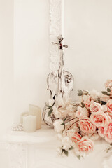 white vintage violin, candles, rose flowers against a white wall with stucco. decor for classic white interior, wedding decor. invitation to a music concert, creative evening