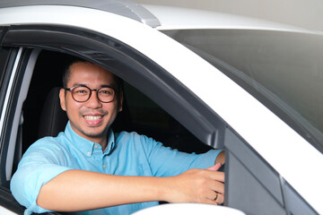 Adult Asian man smiling happy while looking to the camera from inside his car - obrazy, fototapety, plakaty