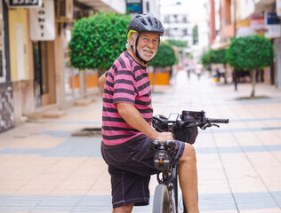 Smiling bearded senior cyclist man on bicycle in city street turns and looks at camera. Active elderly grandfather enjoying a healthy lifestyle and freedom © luciano