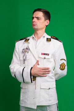 A marine captain wearing a white suit, standing half-turned, isolated on a green background.