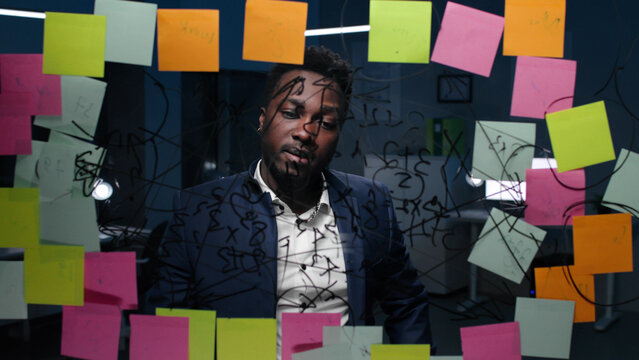 African-American businessman look at glassboard with notes in dark office