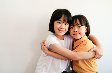 Two girls sitting next to each other hugging each other. showing their connected faces on a white background.