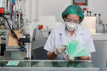 Fototapeta na wymiar Worker woman in personal protective equipment or PPE inspecting quality of mask and medical face mask production line in factory, manufacturing industry and factory concept.