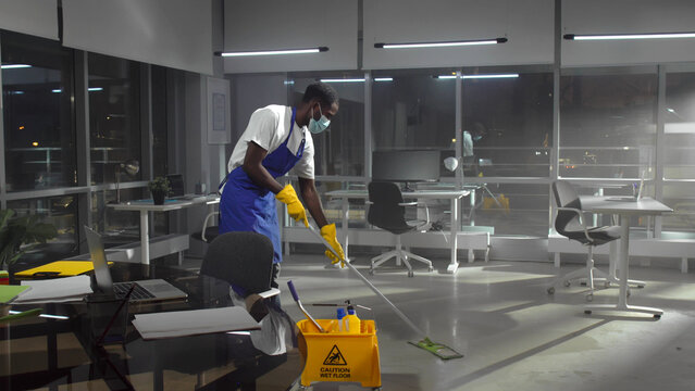 African-American janitor in facemask mop floor in empty office