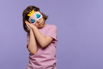 Pretty little girl wearing pink pajamas and sleep mask over lilac background. Child wants to sleep. Copy space. Concept healthy baby sleep. Sweet dreams