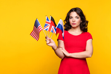 Young woman in red dress shows bunch of diverse flags looking at camera over yellow studio...