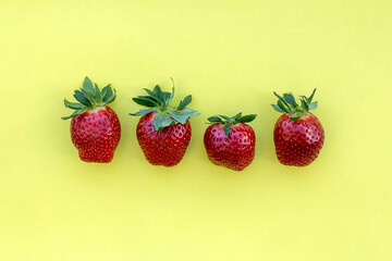 Four fresh red strawberries with green leaves on yellow background  