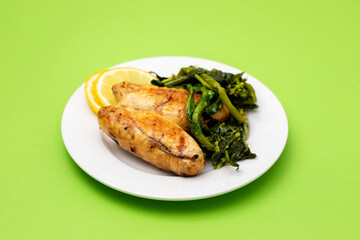 Grilled caviar cod fish with greens and fresh lemon on white small plate.