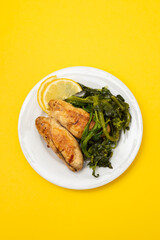 Grilled caviar cod fish with greens and fresh lemon on white small plate.