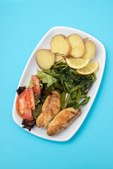 Grilled caviar cod fish with greens and fresh lemon on white small plate.