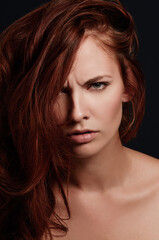 Tempestuous temptress. Closeup portrait of an attractive young redhead in studio scowling at the camera.