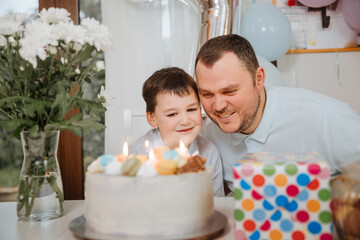 Father with son celebrate children's birthday party at home. Child is 7 years old and blows the...