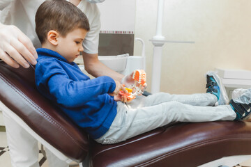 a male dentist shows a boy on a denture how to properly brush his teeth. the concept of children's...