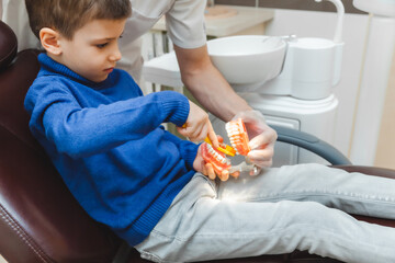 a male dentist shows a boy on a denture how to properly brush his teeth. the concept of children's...