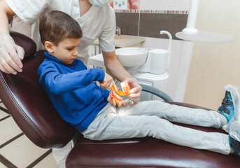 a male dentist shows a boy on a denture how to properly brush his teeth. the concept of children's...