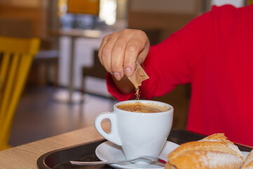 Unrecognizable woman pouring a sugar cube into a cup of coffee, selective focus at hand.