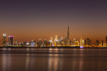 Naklejka premium Dubai Business Bay skyline at night with colorful illuminated buildings and calm Dubai Creek water.