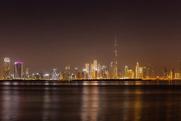Fototapeta na wymiar Dubai Business Bay skyline at night with colorful illuminated buildings and calm Dubai Creek water.