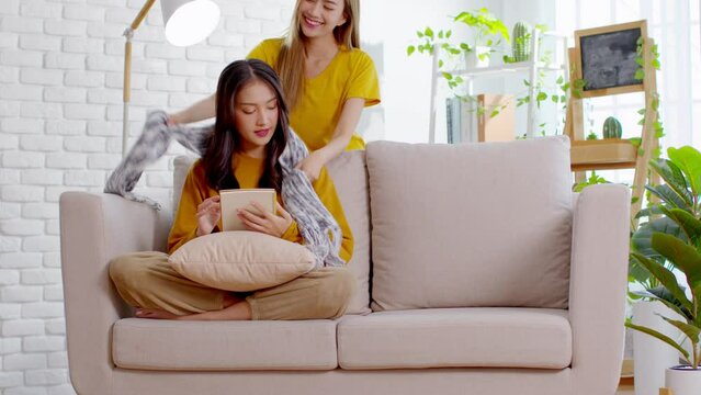 An Asian couple is taking care to their partner. LGBTQ female lasbian give their partner a scarf while the other has reading a book. They are living spending time together.Good moment of LGBTQ