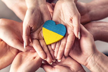 We stand with Ukraine symbol as numerous hands hold one another in unity with a wooden heart...