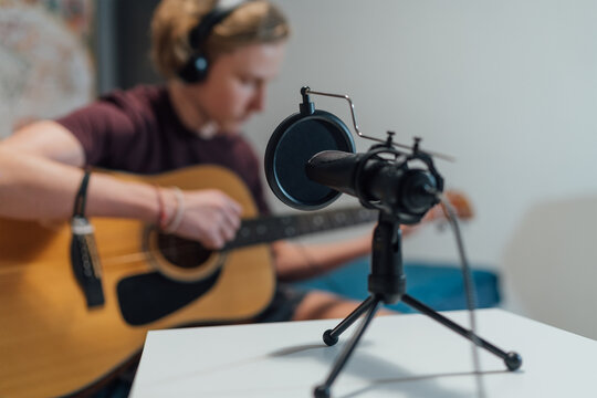 Microphone with pop filter closeup photo with a young teenager boy in headphones recording voice and guitar playing music. Home sound studio audio recording technology and teens hobby concept..