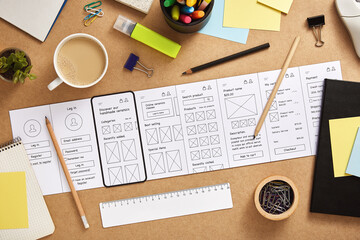 Busy UX designer desk with several mobile app wireframe sketches and office supplies. Top view.