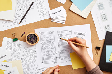 Web UX designer working at desk with several website wireframe sketches and sitemap. Website project concept. Flat lay - obrazy, fototapety, plakaty