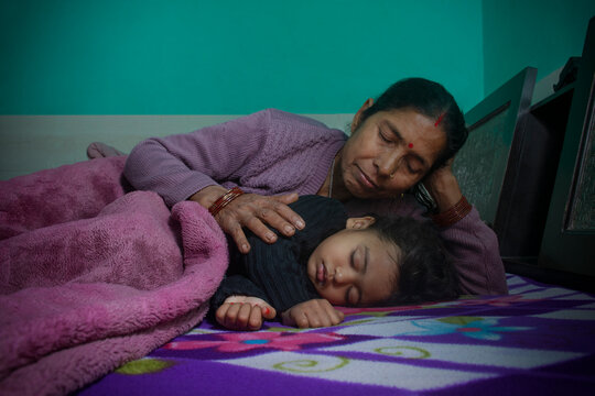 Grandmother and her little granddaughter sleeping together in bed. India