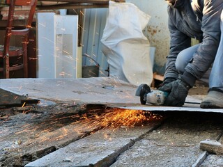 cutting an iron sheet by a grinder in the yard next to the workshop, processing and recycling used metal, a worker cuts iron material with an angle saw with large bright sparks