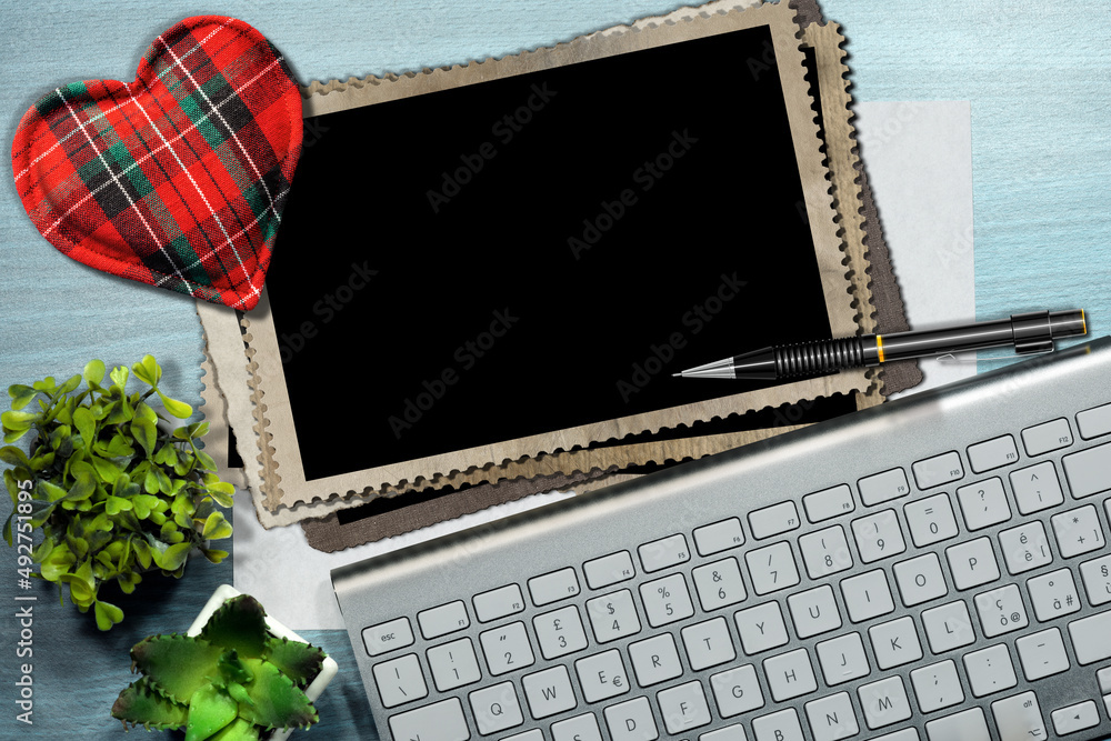 Poster close-up of a fabric heart shape on a stack of vintage and blank photo frames on a desk with a penci