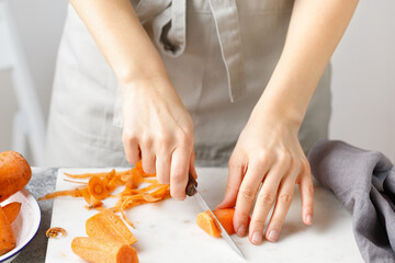 Obraz na płótnie Canvas Hands cut carrot on marble board. Woman in apron cut carrot with peeler. Food preparing. Peel carrot, Vegetable