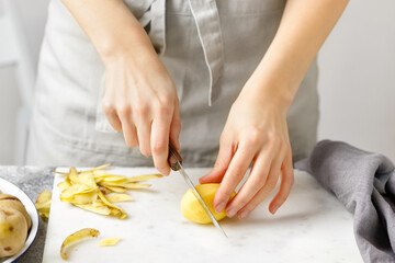 Obraz na płótnie Canvas Hands cut potatoes on marble board. Woman in apron cut potato. Food preparing