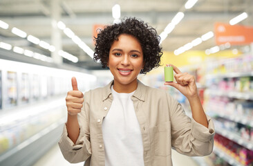 shopping and consumption concept - smiling woman holding alkaline battery over supermarket...