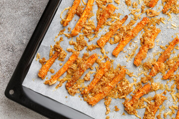 Roasted carrot sticks with cheese and garlic. In a dark square baking tray with paper. Top view