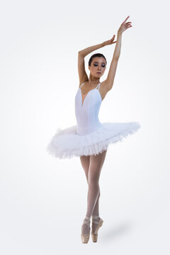 Ballet Dance Concepts. Professional Japanese Female Ballet Dancer Posing in White Tutu With Lifted Hands Against White Background.