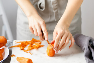 Hands cut carrot on marble board. Woman in apron cut carrot with peeler. Food preparing. Peel...