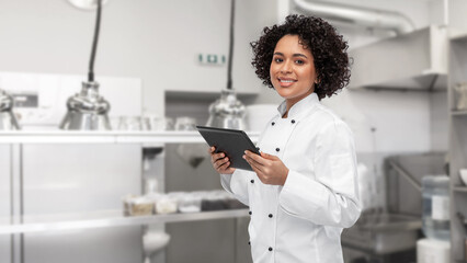 cooking, culinary and people concept - happy smiling female chef in white jacket with tablet pc computer over restaurant kitchen background