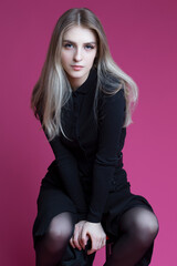 Fototapeta premium Natural Portrait of Sensual Charming Female Blond Girl Posing in Closed Long Black Dress in Studio Against Trendy Pink Background