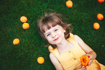 Little girl lying on a grass eating apricot