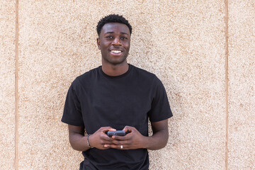 Positive black man using smartphone and smiling at camera on street