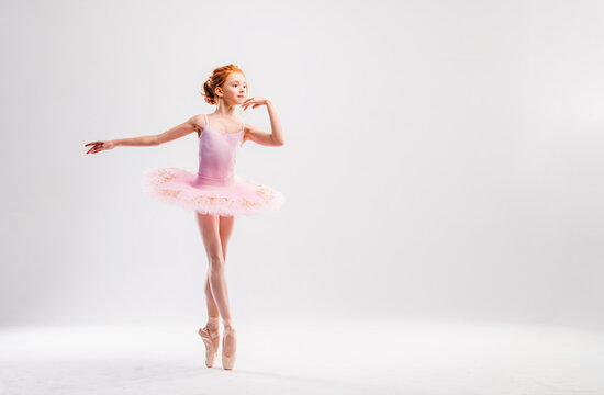 Fototapeta Little ballerina dancer in a pink tutu academy student posing on a white background