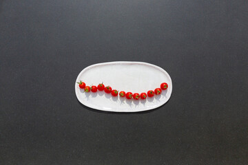 Fresh and tasty cherry tomatoes on white dish on black tabletop. Healthy vegan Food.
