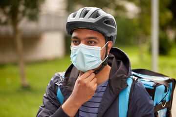 food shipping, health and pandemic concept - delivery man in bicycle helmet and protective medical...
