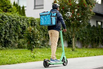 food shipping, transportation and people concept - delivery man in bike helmet with thermal insulated bag riding electric scooter on city street © Syda Productions