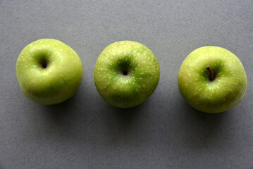 Three delicious green apples on a gray background