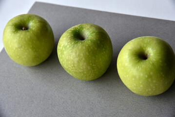 Three delicious green apples on a gray background