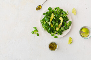 Overhead view of healthy salad with lamb's lettuce, avocado and olive oil on white background