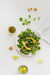 Aerial view of salad with avocado, red onion and lettuce with pesto and walnuts on white background