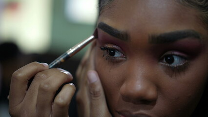 Obraz premium A young black girl applying make-up in front of mirror